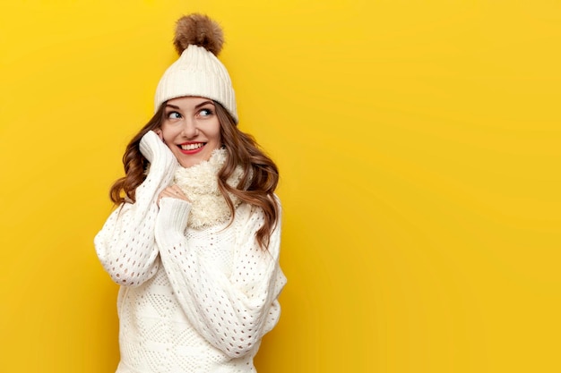 joven linda chica con ropa cálida y suave de invierno sonríe sobre fondo amarillo aislado mujer con sombrero blanco