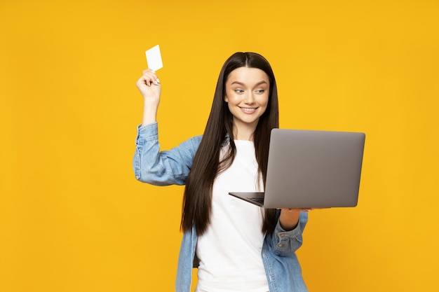 Joven linda con computadora portátil y tarjeta de crédito en las manos