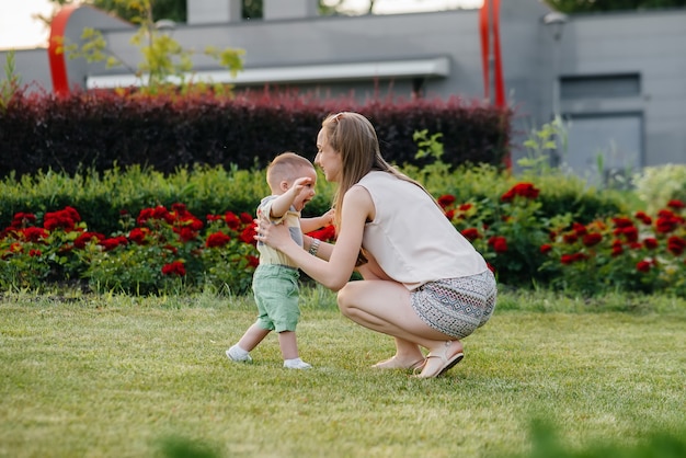 Una joven linda madre ayuda y enseña a su pequeño hijo a dar sus primeros pasos durante la puesta de sol en el parque sobre el césped.