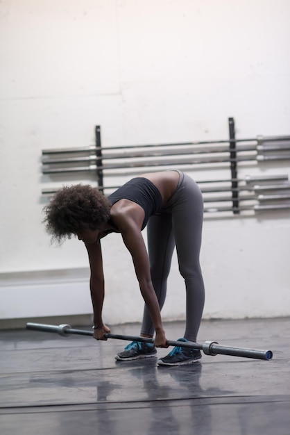 Joven linda mujer afroamericana deportiva en el gimnasio levantando la barra vacía