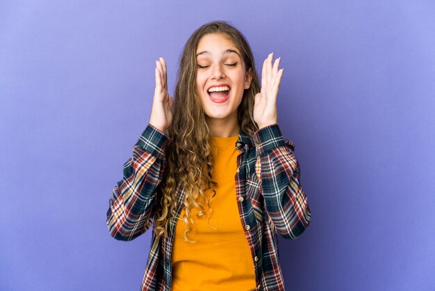 Joven linda mujer caucásica se ríe a carcajadas manteniendo la mano en el pecho