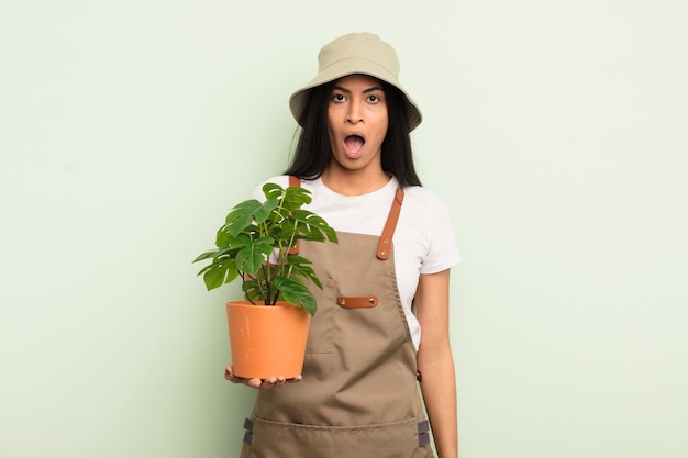 Joven linda mujer hispana que parece muy sorprendida o sorprendida del concepto de agricultor o jardinero