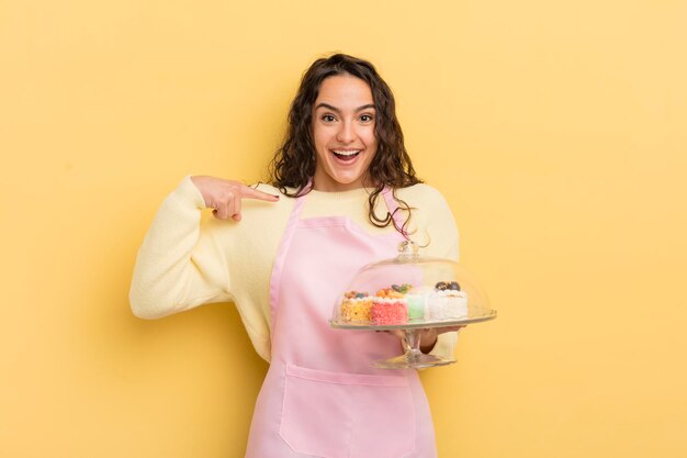 Joven linda mujer hispana que se siente feliz y se señala a sí misma con un concepto emocionado de chef y pasteles