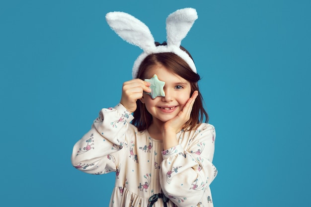 Joven linda niña sonriente usa orejas de conejo cubre ojos con galleta en forma de estrella