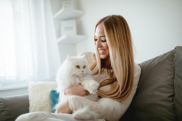 Una joven linda relajándose en casa y sosteniendo a su hermoso gato persa blanco.