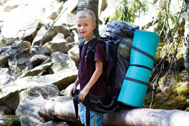 Joven lindo niño feliz niño con mochila turística grande sobre fondo de rocas soleadas