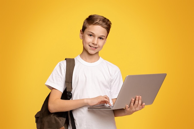 Joven listo para la escuela adolescente con mochila usando portátil panorama de fondo naranja con gratis