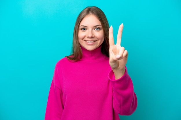 Joven lituana aislada de fondo azul sonriendo y mostrando el signo de la victoria