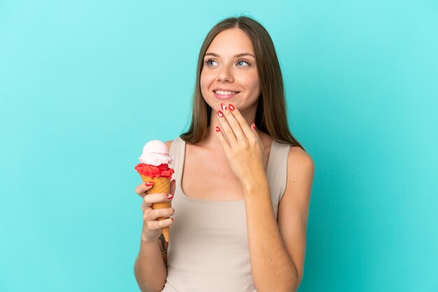 Joven lituana con helado de cucurucho aislado de fondo azul mirando hacia arriba mientras sonríe