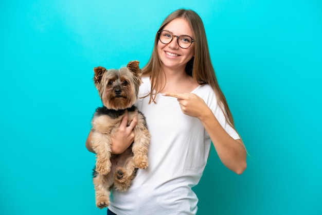 Joven lituana sosteniendo un perro aislado de fondo azul y apuntándolo