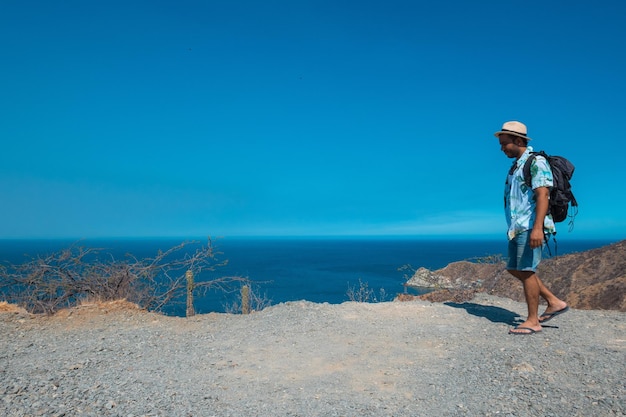 El joven llega a la cima de la montaña, la roca y disfruta del hermoso sol que brilla