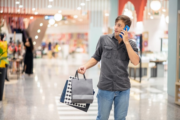 Un joven lleva en la mano muchos paquetes de compras, camino por el centro comercial, hablando por teléfono y mirando a un lado. Concepto de compras. Viernes negro