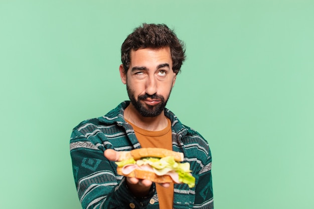 Joven loco con barba expresión triste y sosteniendo un sándwich