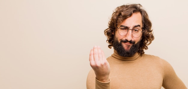 ¡Un joven loco con barba que hace gestos de dinero o capice, diciéndole que pague sus deudas! contra la pared de color plano