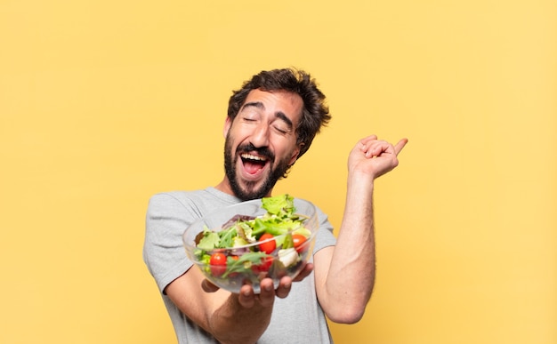 Joven loco barbudo a dieta celebrando una victoria exitosa y sosteniendo una ensalada