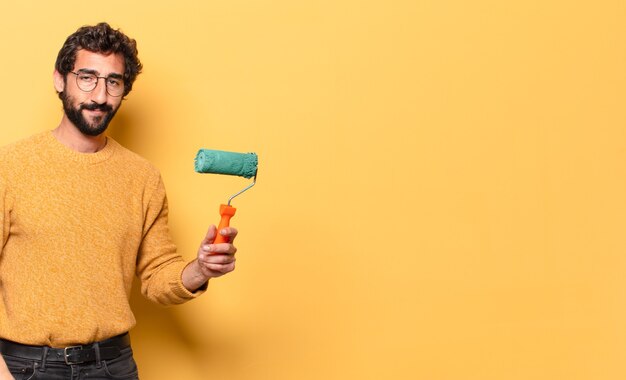 Joven loco barbudo con un rodillo de pintura pintando y cambiando el color de la pared