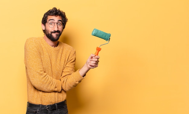 Joven loco barbudo con un rodillo de pintura pintando y cambiando el color de la pared