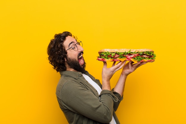 Joven loco barbudo con un sándwich gigante.