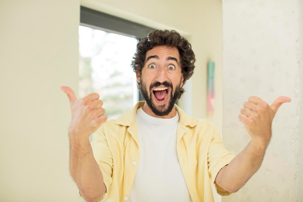 joven loco barbudo sonriendo alegremente y luciendo feliz, sintiéndose despreocupado y positivo con ambos pulgares hacia arriba