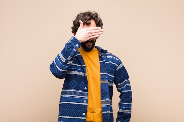 Joven loco loco cubriendo los ojos con una mano sintiendo miedo esperando una sorpresa contra la pared plana