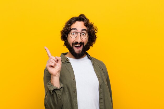 Joven loco que se siente como un genio feliz y emocionado después de darse cuenta de una idea, levantando alegremente el dedo, ¡eureka! contra la pared amarilla