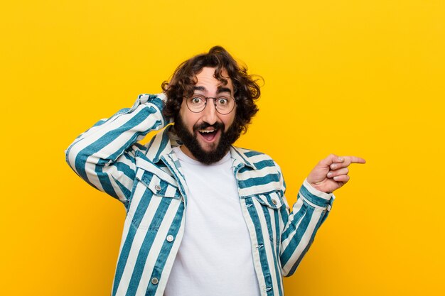 Joven loco riendo, feliz, positivo y sorprendido, dándose cuenta de una gran idea apuntando al espacio lateral de la copia pared amarilla