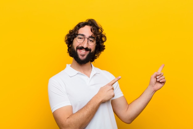 Joven loco sonriendo alegremente y apuntando hacia un lado y hacia arriba con ambas manos mostrando el objeto en la pared amarilla copyspace