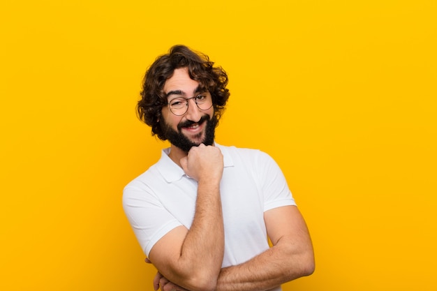 Joven loco sonriendo, disfrutando de la vida, sintiéndose feliz, amigable, satisfecho y despreocupado con la mano en la pared de la barbilla amarilla