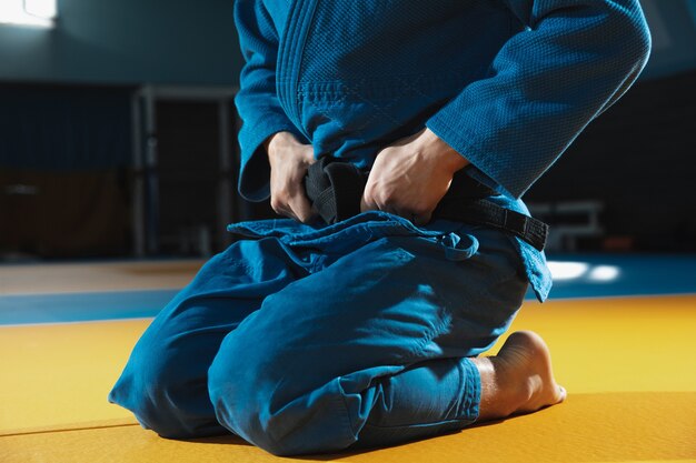 Joven luchador de judo en kimono posando cómodo en el gimnasio fuerte y saludable