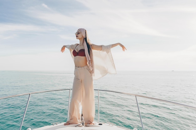 Una joven lujosa con ropa de verano elegante posando en su barco blanco navegando hacia la isla