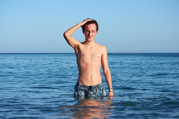 Un joven macho caucásico en forma posando y tocando su cabello en el mar