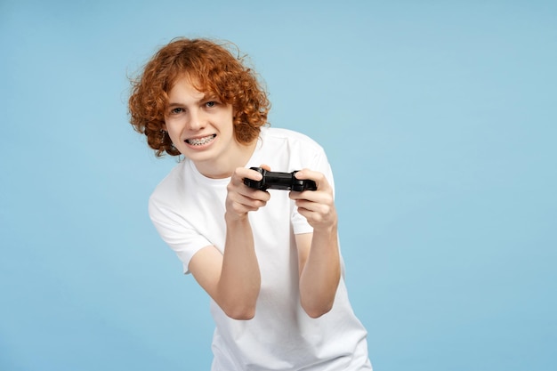 Un joven macho concentrado con cabello pelirrojo rizado y aparatos ortopédicos se involucra con un controlador de juego