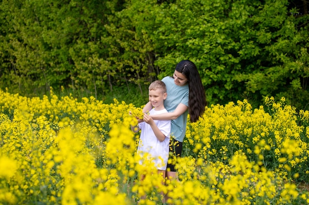 Una joven madre abraza a su hijo en un campo con flores amarillas.