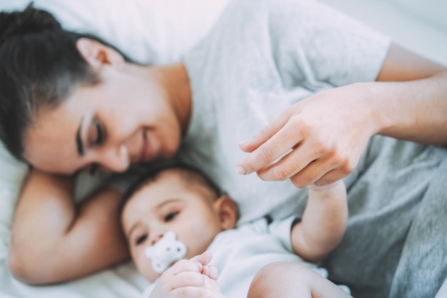 Joven madre acostada en la cama con su hijo en la cama en casa - Centrarse en la mano de mamá