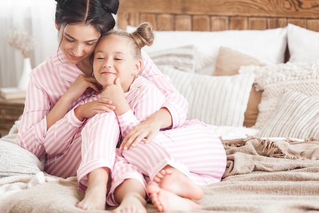 Joven madre activa y su pequeña hija divirtiéndose juntos en casa en el dormitorio vistiendo pijamas