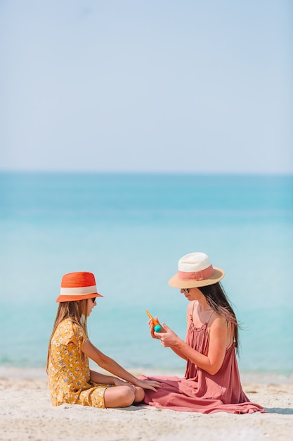 Joven madre aplicando crema solar a la nariz de la hija en la playa