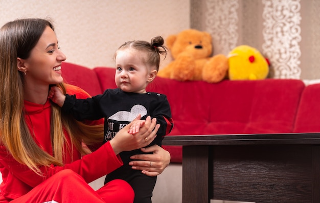 Joven madre apoyando a su pequeña hija de pie riendo como la pequeña niña