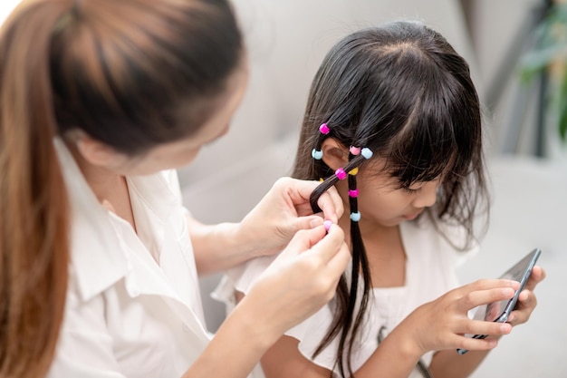 Joven madre asiática atando el cabello de su hija