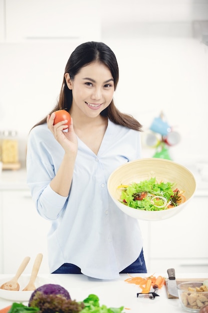 Joven madre asiática haciendo comida en la cocina con cara de sonrisa.