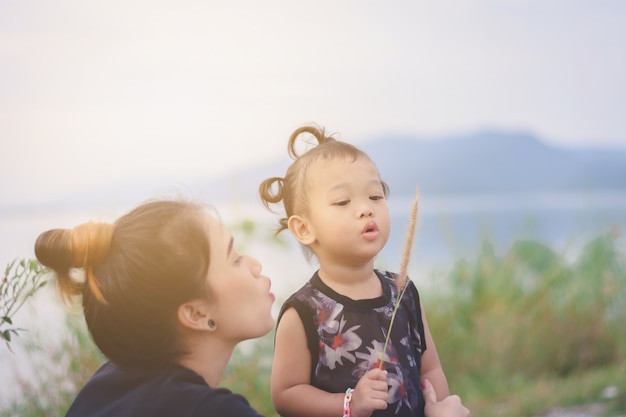 Joven madre asiática con niño lindo y dulce jugando al aire libre con la flor de la hierba
