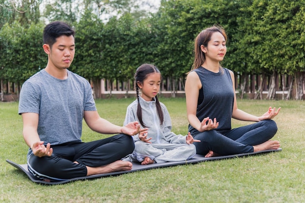 Joven madre asiática, padre practicando ejercicios de yoga con su hija al aire libre en una pose de meditación juntos en la naturaleza, un parque de jardín, deporte familiar para niños y ejercicios para un estilo de vida saludable