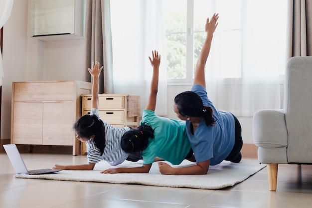 Joven madre asiática y sus hijas haciendo estiramientos ejercicios de fitness yoga juntos en casa. Los padres y los niños se esfuerzan por mantenerse fuertes y mantener la salud física y el bienestar en la rutina diaria.