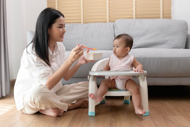 Joven madre ayudando al bebé a comer alimentos combinados en una silla para bebés