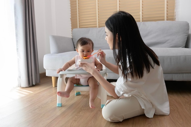 Joven madre ayudando al bebé a comer alimentos combinados en una silla para bebés