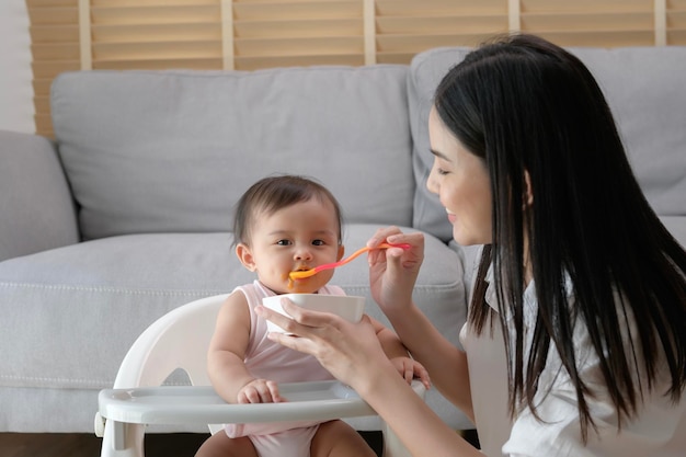 Joven madre ayudando al bebé a comer alimentos combinados en una silla para bebés