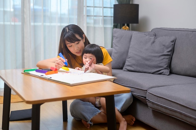 Una joven madre ayudando a su hija a dibujar con lápices de colores en la sala de estar de casa.