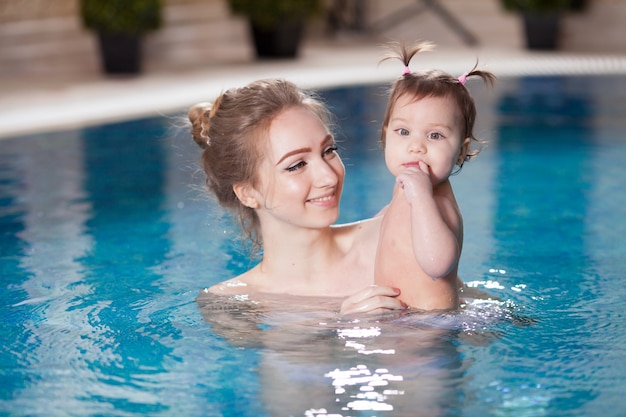 Joven madre baña al bebé en la piscina.