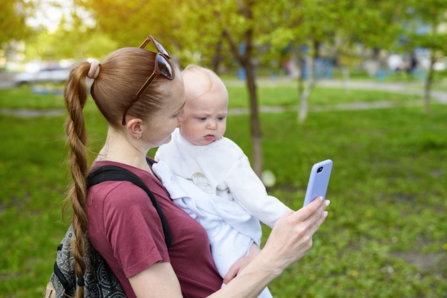 Joven madre con un bebé en brazos usando un teléfono inteligente