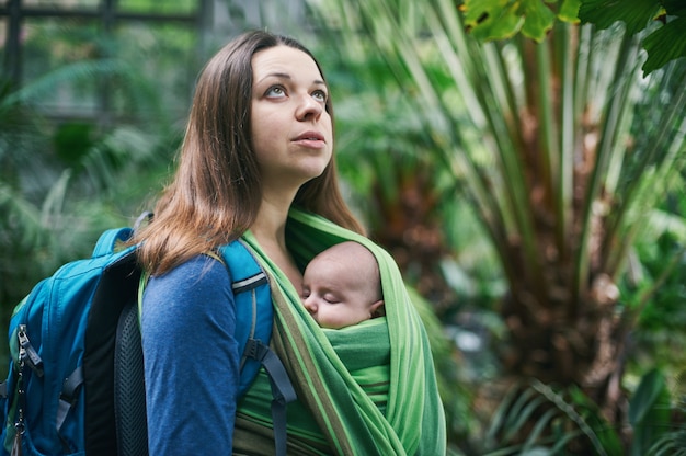 Una joven madre con un bebé en una honda está caminando en la jungla