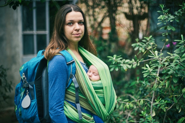 Una joven madre con un bebé en una honda está caminando en la jungla